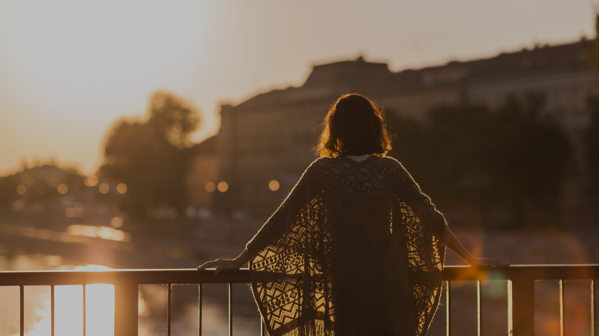 kobieta stoi tyłem do obiektywu, patrzy na zachód słońca